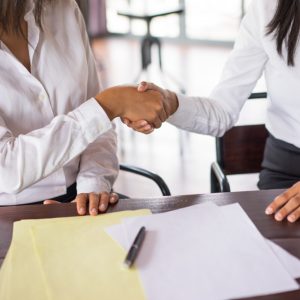 closeup-two-business-women-shaking-hands-sitting-desk